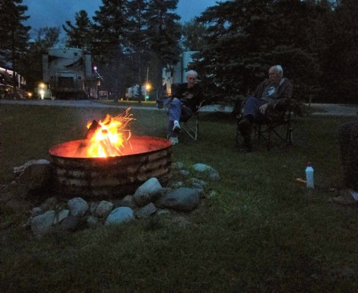 Two people sitting next to a campfire.